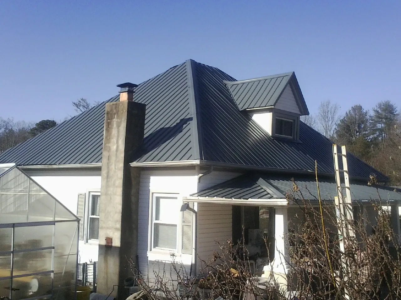 Dark blue standing seam metal roof on a white farmhouse with dormer — Slate & Tile Roof Repair by Roofing Brothers in Rio Grande
