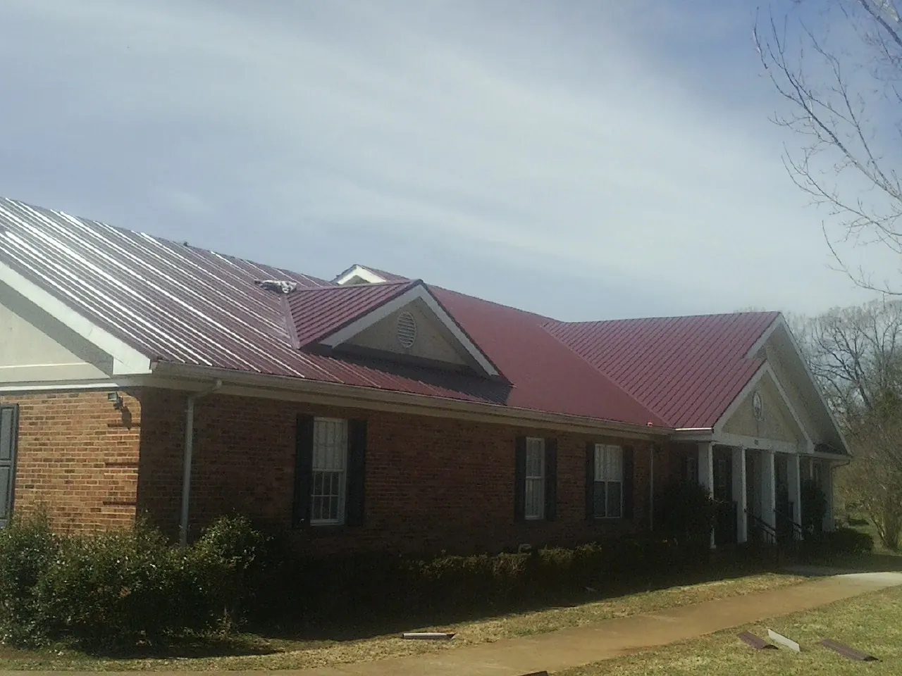 Red metal roof with gabled entries on a long brick building, from a Hail Damage Roof Repair job in Rio Grande