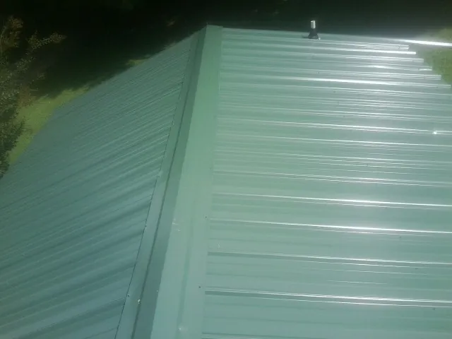 New green metal panels meeting at the ridge of a roof — Flat Roof Repair work by our crew in Rio Grande