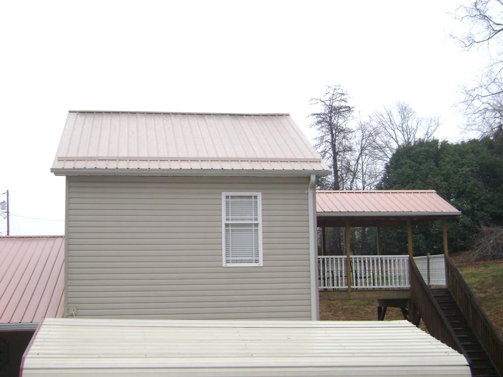 Tan metal roofs on a two story addition and attached porch, from a Roof Replacement job in Rio Grande